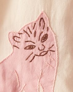 a close up of a cat embroidered on a pink t - shirt with white background