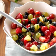 a white bowl filled with fruit on top of a wooden table next to a fork