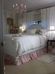 a white bed with pink ruffled bedspread and chandelier hanging from the ceiling