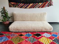 a white couch sitting on top of a red rug next to a potted plant