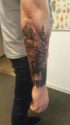 a man with a mountain and trees tattoo on his arm