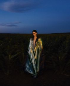 a woman standing in the middle of a corn field at night wearing a blue and gold dress