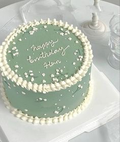 a green birthday cake with white frosting on a table next to some wine glasses