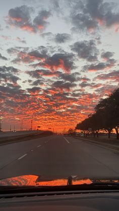 the sun is setting on an empty road with trees in the distance and clouds in the sky