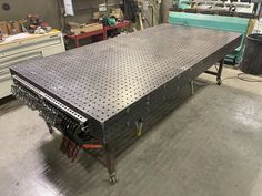 a large metal table in a garage with lots of tools on the floor and workbench behind it