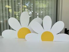 two white and yellow paper flowers sitting on top of a table next to a window