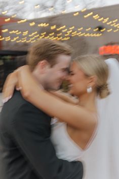 a bride and groom hugging each other in front of a building with lights on it