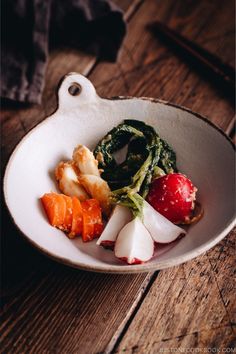 a white bowl filled with vegetables on top of a wooden table