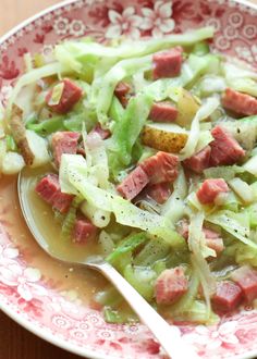 a bowl filled with meat and vegetables on top of a wooden table next to a spoon