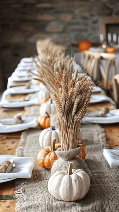 the table is set with white pumpkins and wheat stalks in vases on burlap