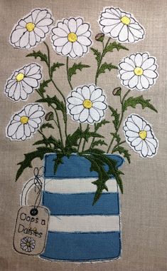 a blue and white striped vase filled with daisies on top of a beige background