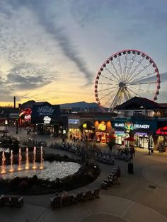 an amusement park at dusk with ferris wheel in the foreground and lights on display