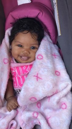 a baby in a car seat with a pink blanket on it's head and smiling