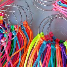 several pairs of hoop earrings with multi colored thread and beads hanging from metal hooks on a white surface