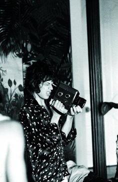 black and white photograph of a woman holding an old camera in front of her face