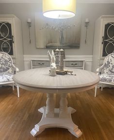 a white table and chairs in a room with wood floors, an oval mirror on the wall