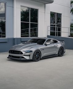 a silver mustang parked in front of a building with windows and palm trees behind it