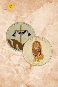 two circular badges with lions on them sitting on top of a marble surface, one is gold and the other is brown