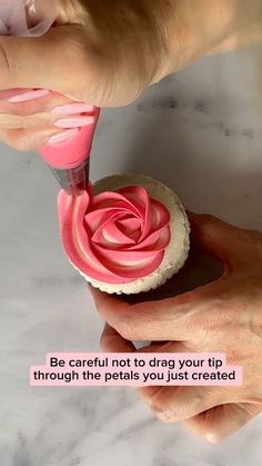 someone is decorating a cupcake with pink icing