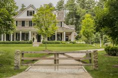 a large white house in the middle of a lush green yard with a wooden gate