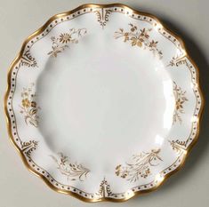 a white plate with gold trimmings and flowers on the rim, against a gray background