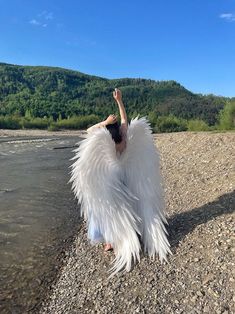 a woman with white wings is standing in the water and holding her arms up to the sky