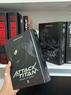 a person holding up a book in front of bookshelves with red and black covers