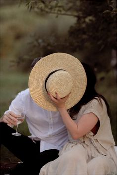 a woman sitting on the ground wearing a straw hat and holding a glass of wine