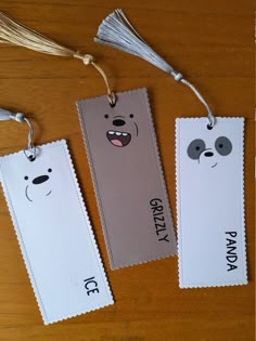 three bookmarks with faces on them sitting on top of a wooden table next to tassels