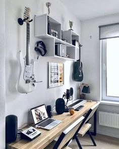 a laptop computer sitting on top of a wooden desk next to a guitar hanging from the wall