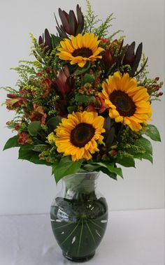 a vase filled with lots of yellow sunflowers on top of a white table