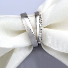 two wedding bands with diamonds on top of each other, sitting next to a white bow