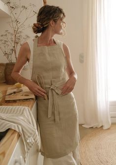 a woman standing next to a counter in a kitchen wearing an apron and holding a pair of scissors