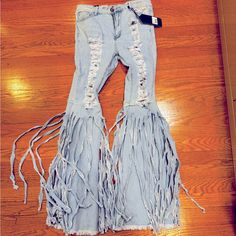 a pair of light blue jeans with fringes on the bottom and sides, sitting on a wooden floor