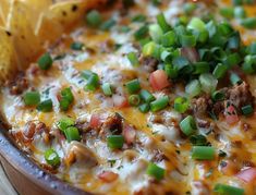 a casserole with meat, cheese and green onions in a bowl next to a tortilla chip