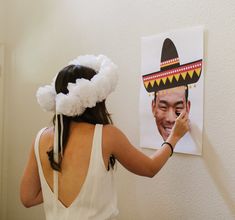 a woman in a white dress painting a picture on the wall with a black and red sombrero