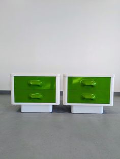 two green and white nightstands sitting side by side on cement floored area with wall in background