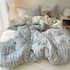 an unmade bed with blue and white striped comforter, pillows and stuffed animal