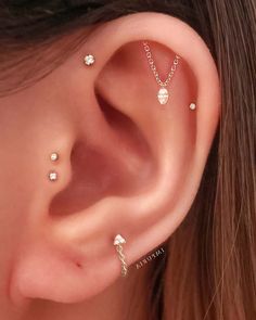 a woman wearing three different piercings on her ear and behind the ear is a gold chain