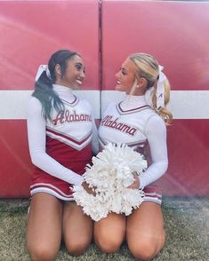 two cheerleaders sitting on the ground with pom poms in their hands