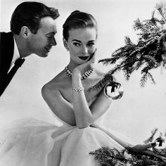 a man looking at a woman in a ball gown next to a christmas tree with ornaments on it