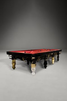 a pool table with red cloth and gold trimmings on the legs, in front of a gray background