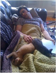 a man laying in bed with two cats sleeping next to him and reading a book