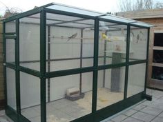 a large green cage with birds in it on top of a tiled floor next to a building