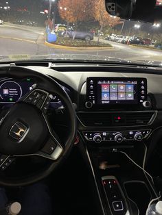 the interior of a car with dashboard, steering wheel and display screen showing cars driving on a city street at night