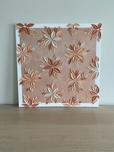 a pink and gold flowered paper art on a wooden table with a white wall in the background