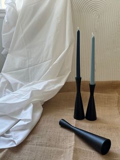 two black candles sitting next to each other on top of a tablecloth covered floor