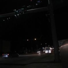 a dark street at night with cars parked on the side of the road and traffic lights above