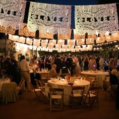 a group of people standing around tables with lights hanging from the ceiling and paper lanterns above them