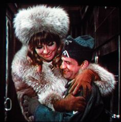 a man holding a woman in his arms while she is wearing a fur coat and hat